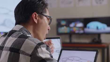 close up  side view of asian male yawning while drawing new car design concept on a tablet in the studio with tv and computers display 3d electric car model