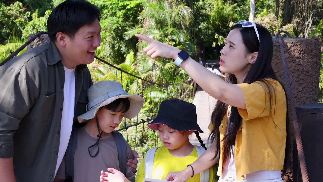 พ่อแม่และเด็กชาวไทยดูแผนที่กระดาษด้วยกันระหว่างเดินป่าในป่าที่แดดส่อง