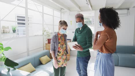 office colleagues wearing face mask discussing over digital tablet at office