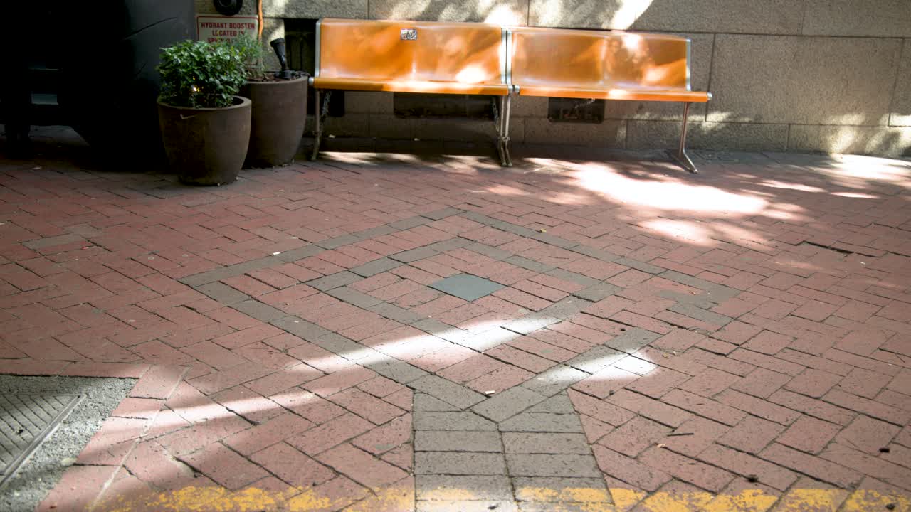 Several adults entering from left, walking across brick past orange bench and pots to cross