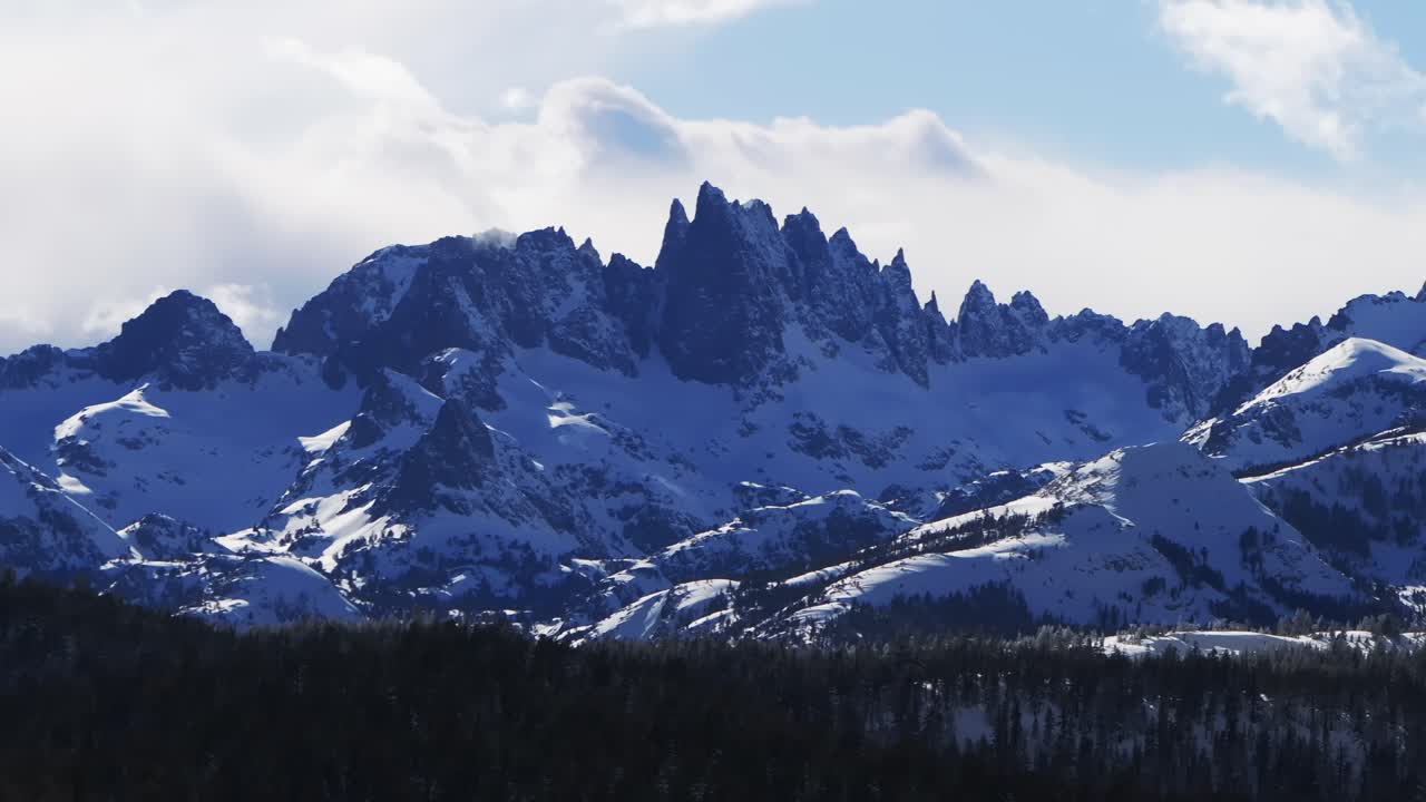 The Hemlocks Mammoth Mountain ski snowboard resort winter sunny blue sky afternoon aerial drone California The Minarets jagged towering peaks fresh deep snow clouds Inyo National Forest static shot