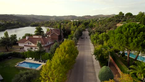 Scenic-aerial-view-of-a-motorcyclist-appearing-riding-down-a-straight-road-in-an-upscale-lakeside-development-at-sunset