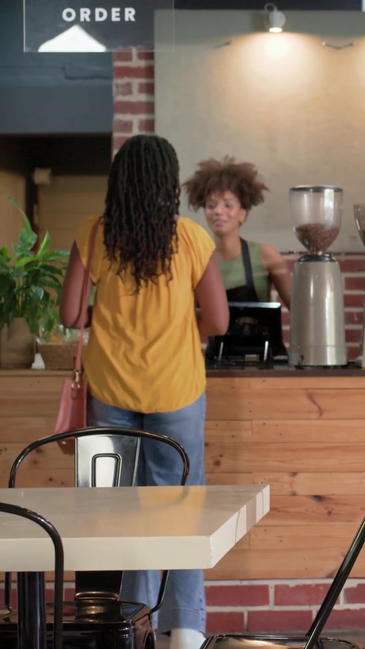 Video verticale: Entrando in un caffè, una donna con un top giallo trascina una borsa, ordina e paga al terminale POS.