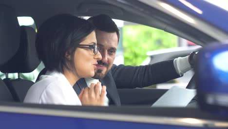 elegant man sitting in car salon and talking with female car dealer. young confident guy choosing automobile in showroom