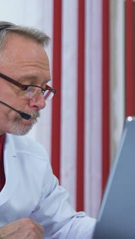 doctor talking in video chat from office. senior doctor sitting at desk and talking to camera. vertical video