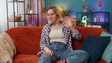 Portrait-of-young-woman-smiling-at-camera-and-waving-gesturing-hello-hi-greeting-or-goodbye-at-home