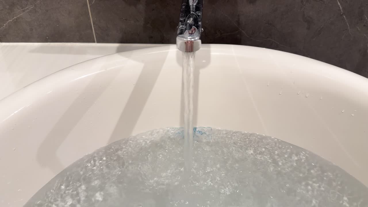 Un getto d'acqua continuo riempie una vasca da bagno ovale bianca in un lussuoso bagno moderno.