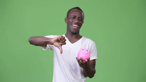 young african man holding piggy bank and giving thumbs down