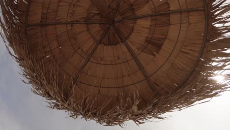 a brown beach sun umbrella on a gentle breeze during a sunny summer day