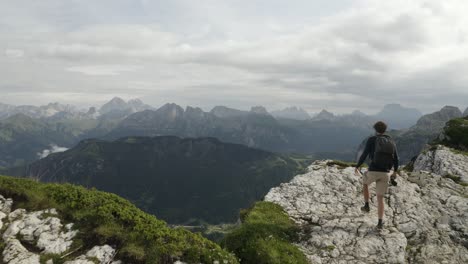 epic man adventurer walks up to a cliff ridge to have a beautiful view vista in mountain backdrop, alleghe, refugio tissi, italy