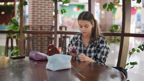 la dama aplica con bastante cuidado el maquillaje en la frente usando la base mientras está sentada en una mesa de madera, varios productos de belleza, un espejo y una bolsa de cosméticos están ordenadamente dispuestos