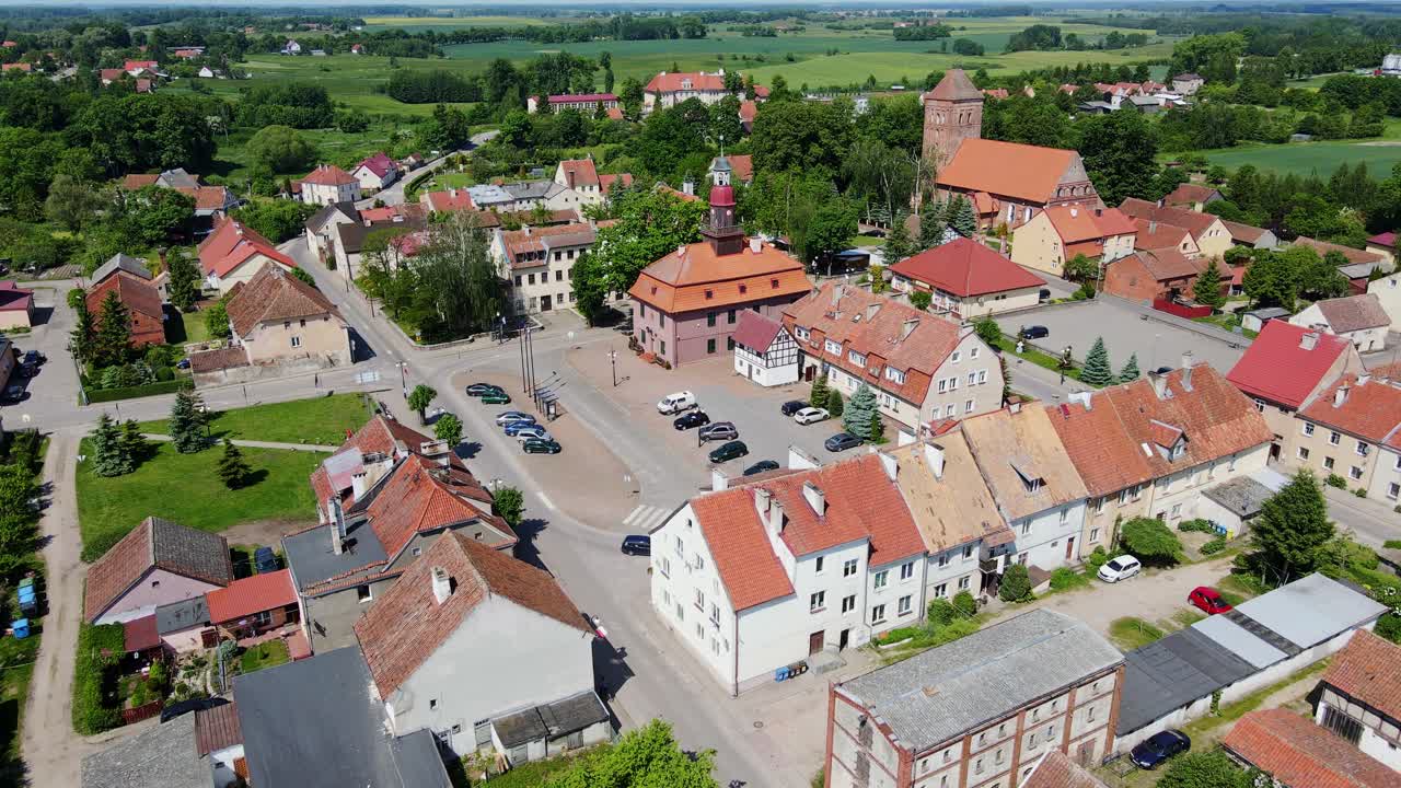 Scenic Srokowo village square, red-roofed buildings nestled, lush Polish nature