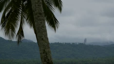 a huge rock formation in the distance behind the beautiful landscape in são tomé island - time lapse