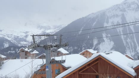 Empty-chairlift-running-in-ski-station-with-nobody-on-it,-and-overcast-weather-in-the-moutains-behind