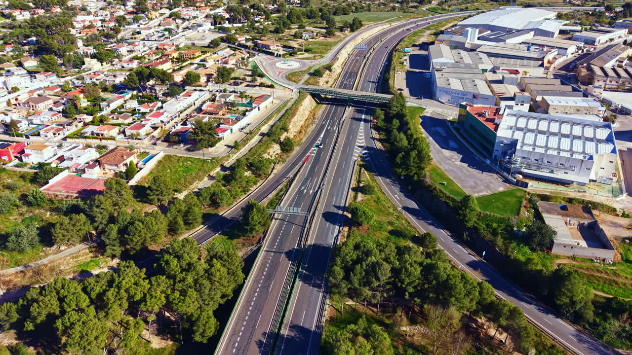 Il traffico scorre su un'autostrada trafficata vicino a una città con spazi verdi ed edifici industriali di giorno.