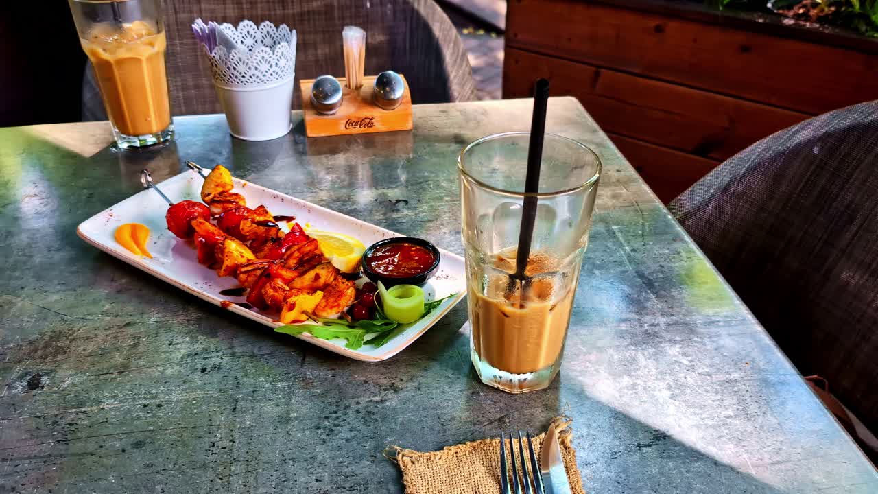 Tasty grilled skewers served with dip, fresh vegetables, and iced coffee at a relaxing café