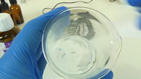 a video showcasing the process of shaking a clear, transparent serum in a glass beaker in a professional cosmetic laboratory.