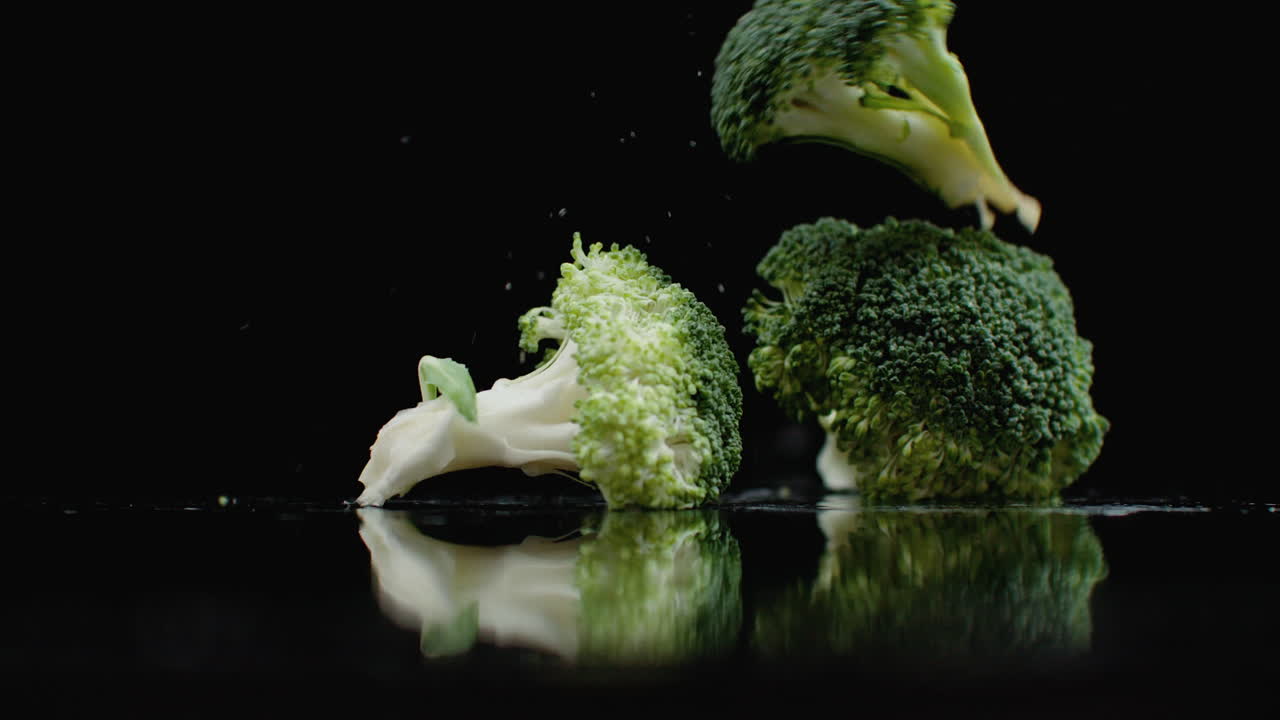 A lot of green fresh broccoli fall on a glass with splashes and drops of water in slow motion on a dark background. Ingredients for Salad Healthy Food.