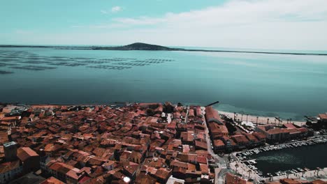 aerial shot with a drone of a small town in the south of france at the edge of a pond with an oyster farm in the background on the left, the sea on the horizon, a port