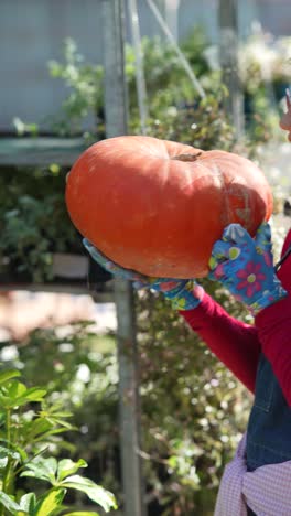 mujer sosteniendo una gran calabaza naranja en un centro de jardinería o mercado