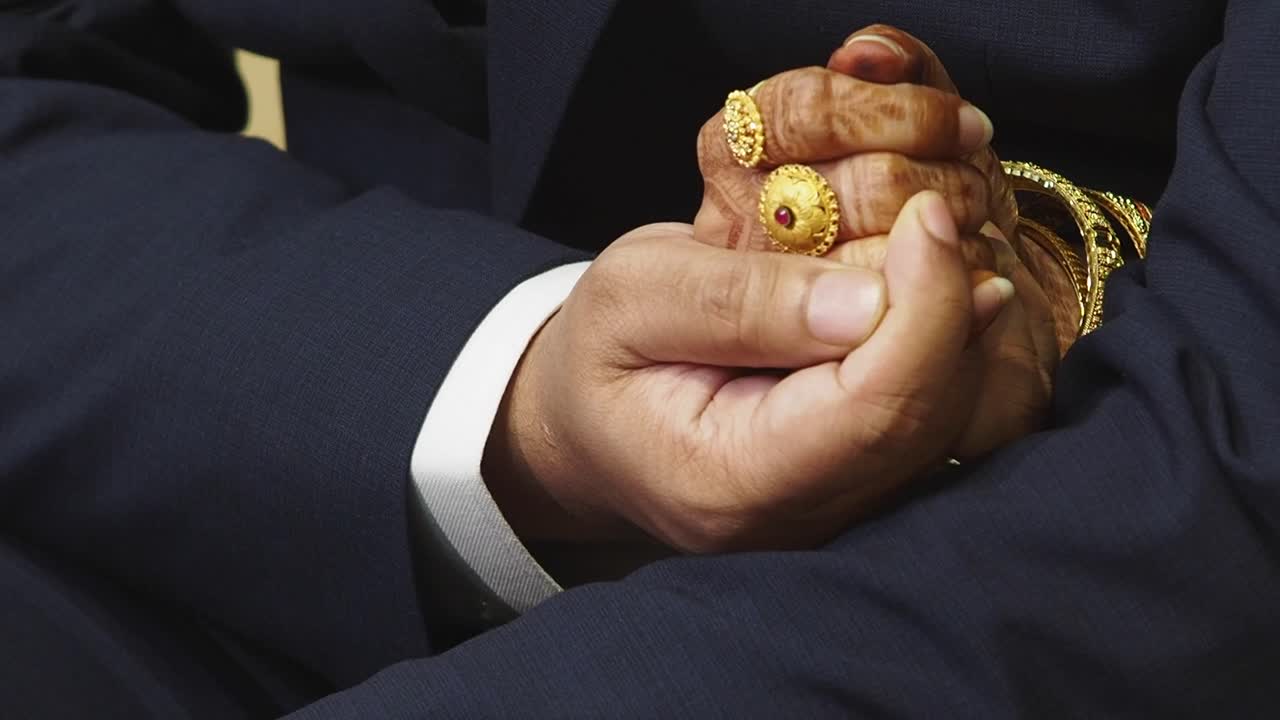 Par der holder i hånd, iført ringe og guldsmykker
