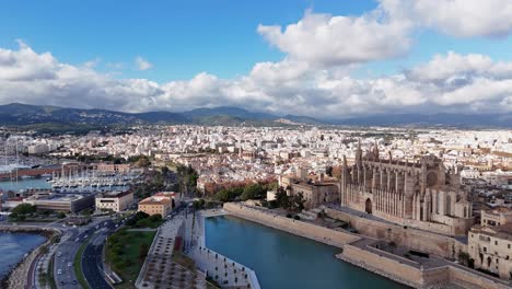 Toma-Aérea-De-Establecimiento-Que-Muestra-El-Tráfico-En-La-Carretera-Costera-Y-La-Famosa-Catedral-De-Mallorca-En-La-Ciudad-De-Palma