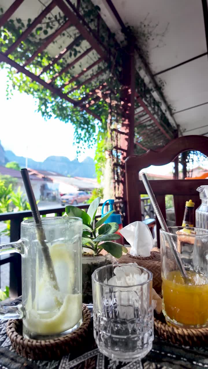 Multiple empty drink glasses sitting on a wicker tray on an outdoor cafe table in Vang Vieng. vertical video