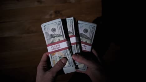 las manos masculinas sostienen tres pilas de billetes de 10.000 dólares en un fondo de madera.