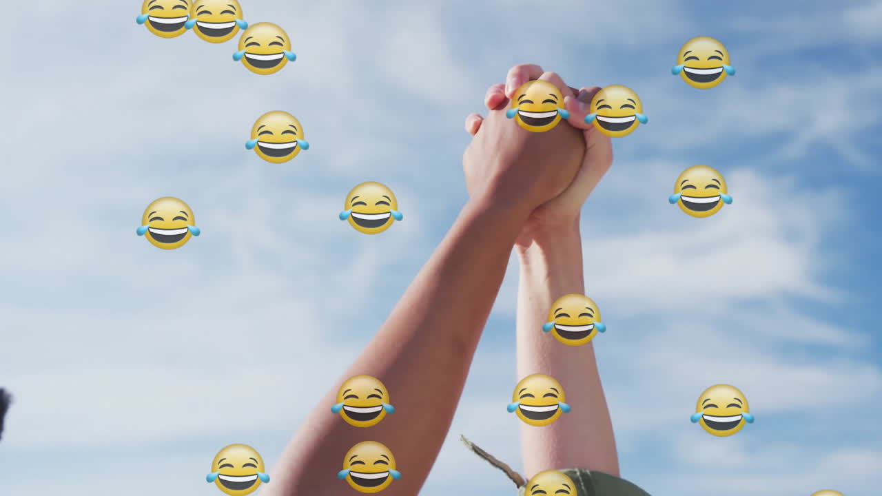 Women raising clasped hands outdoors, with floating emojis illustrating business unity concept