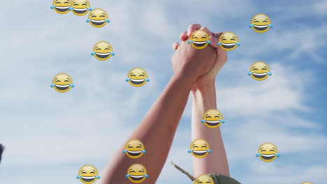 women raising clasped hands outdoors, with floating emojis illustrating business unity concept