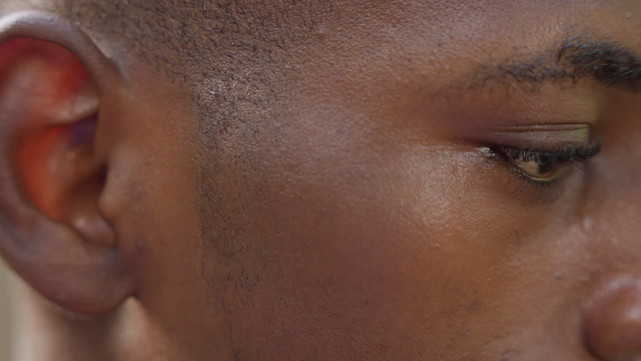 Close up profile black man contemplative gaze, soft natural lighting reveals skin texture and quiet sheen, eyes lowered in focused reflection, slight jaw tension and subtle expression conveying