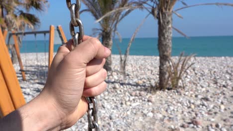 Person-holding-on-the-swing-chain-on-the-beach,-beautiful-view-of-the-sea-that-disappears-on-the-horizon