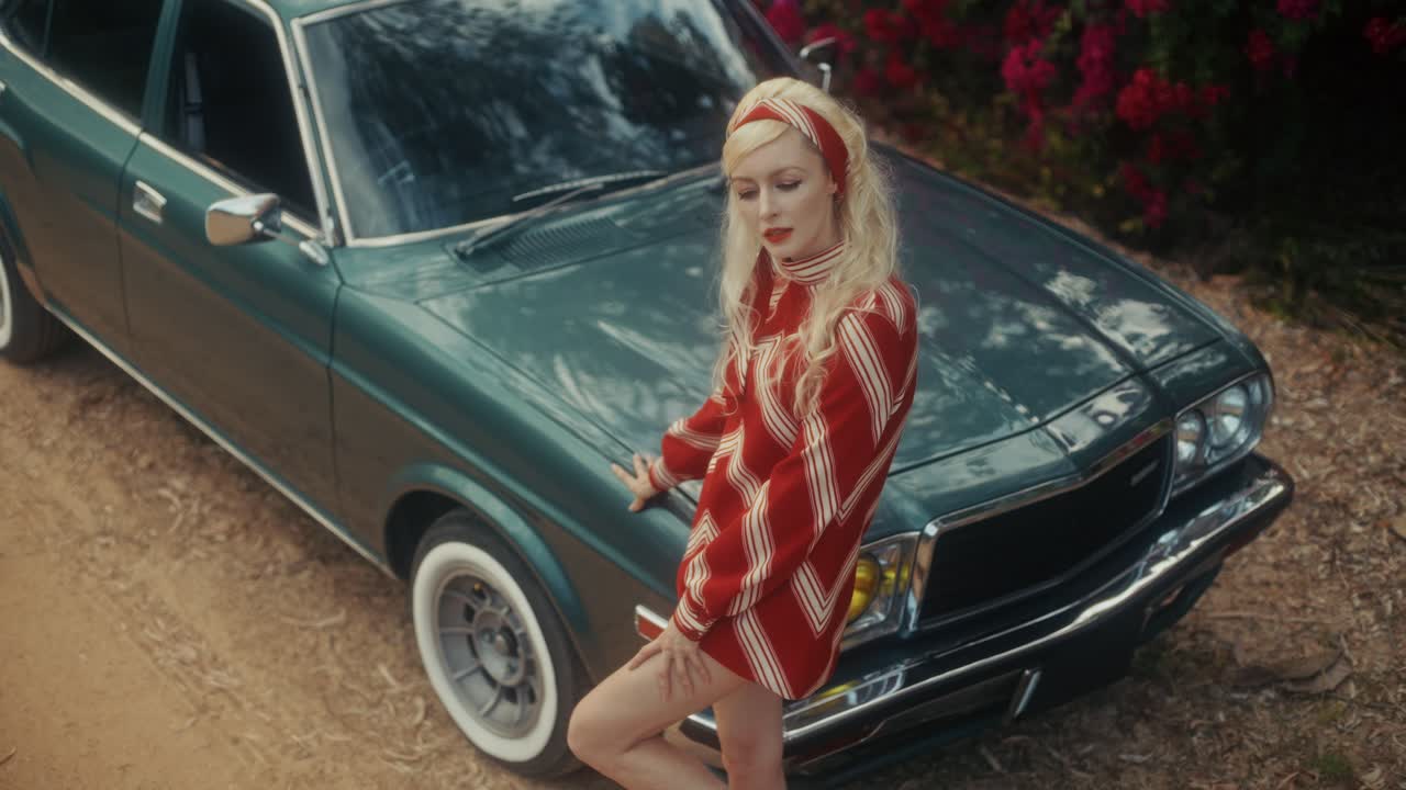 Donna bionda alla moda che posa con un'auto verde d'epoca