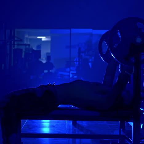 handsome young man steping up for doing bench press workout in gym. blue light filter. video from the side.