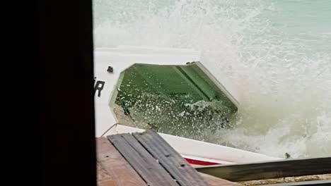 close up pan of local wooden fishing boat being smashed into pieces during sudden storm with rough waves, caribbean