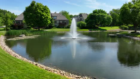 Drone-view-zooming-in-on-townhomes-in-a-private-community-with-a-park-like-setting,-a-small-lake-and-a-fountain