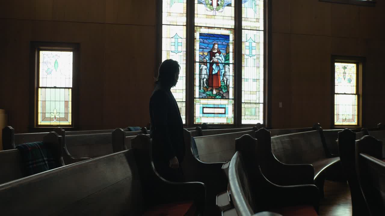 Interior of a quiet church sanctuary with rows of wooden pews and a large stained-glass window at the front, symbolizing peace and faith
