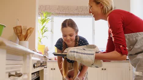 Mother-removing-freshly-baked-cookies-out-of-the-oven-while-daughter-smelling-it-4K-4k