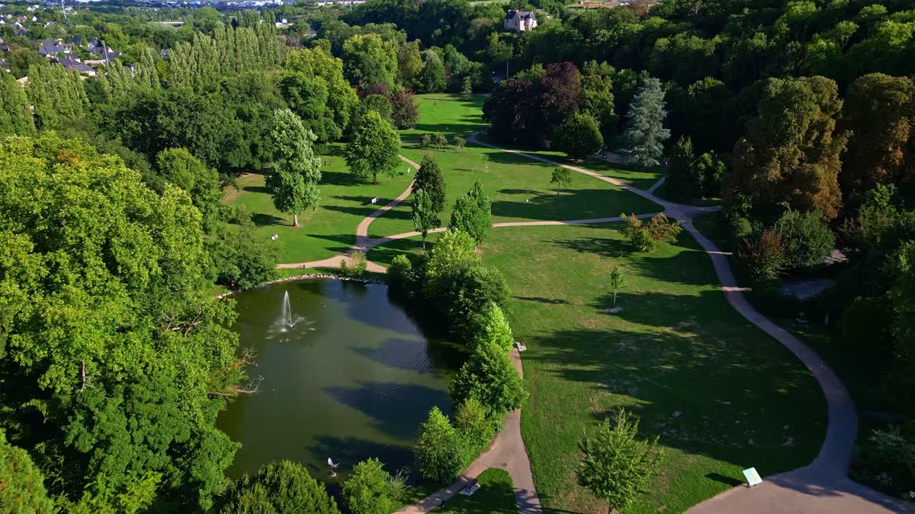 Parc des Ondines, Changé, France, lake with fountain, green lawns, and lush trees on sunny day. Aerial forward