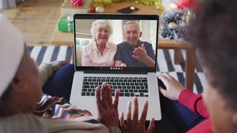 african american mother and daughter using laptop for christmas video call with couple on screen