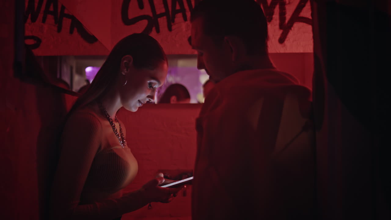 Couple enjoy intimate conversation in neon-lit nightclub with graffiti closeup