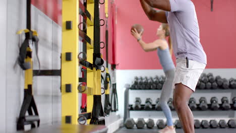 fit african american man and young caucasian woman exercising at the gym with medicine ball