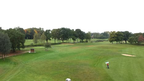 two people walk through the fairway of a golf course with umbrellas