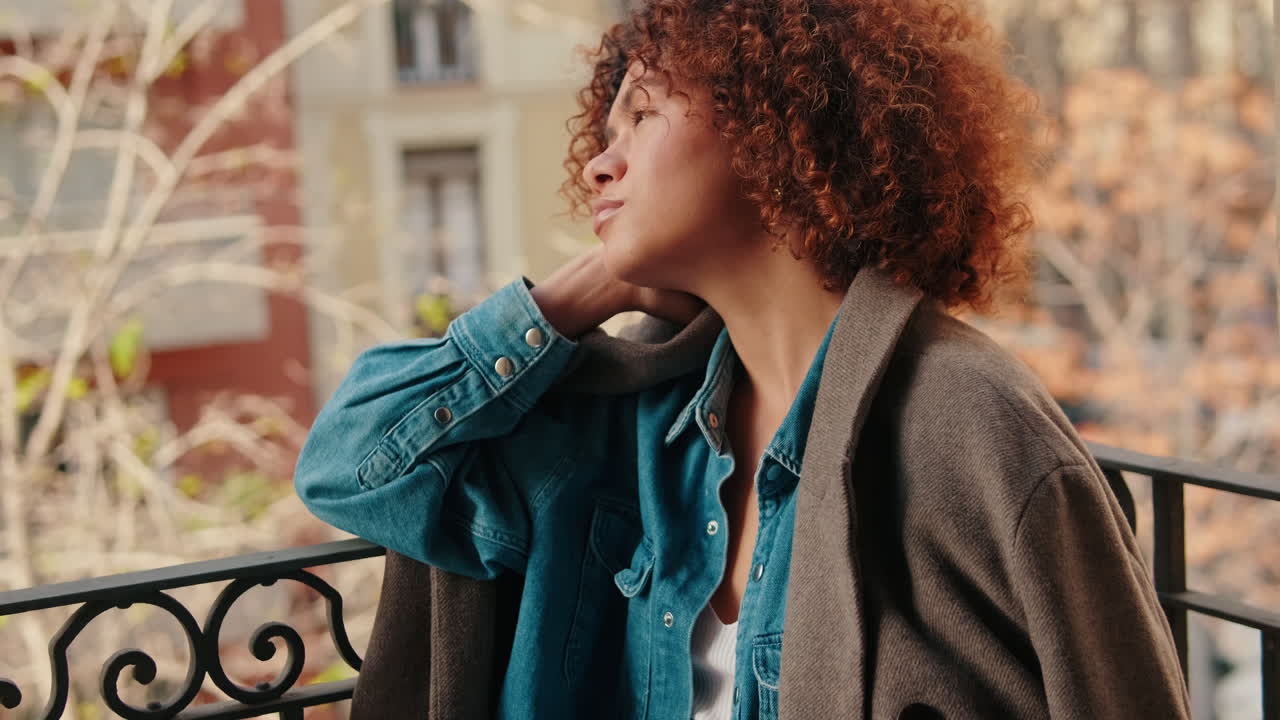 Young Woman with Curly Hair Relaxing on Balcony in Sunlight