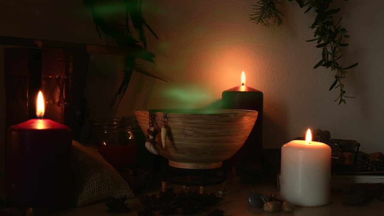 detalle de una poción que hace una habitación de brujas, con vapor verde saliendo de un cuenco de madera, dientes de animales colgando de él, velas con llamas parpadeantes, libros viejos, vasos y hierbas, polvo volando alrededor