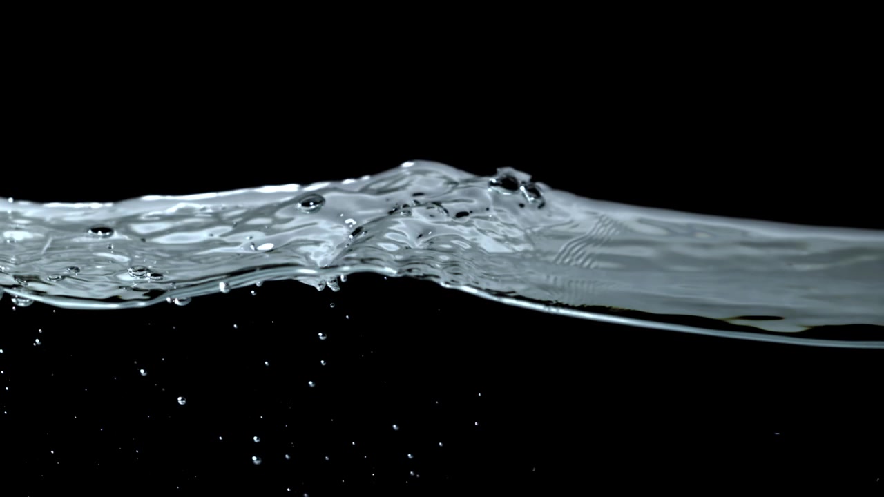 Superficie dell'acqua in movimento lento con increspature e bolle su sfondo nero.