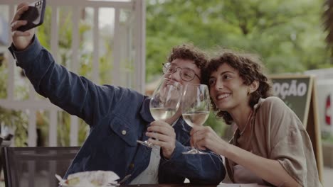 happy couple taking a selfie with wine glasses at an outdoor cafe