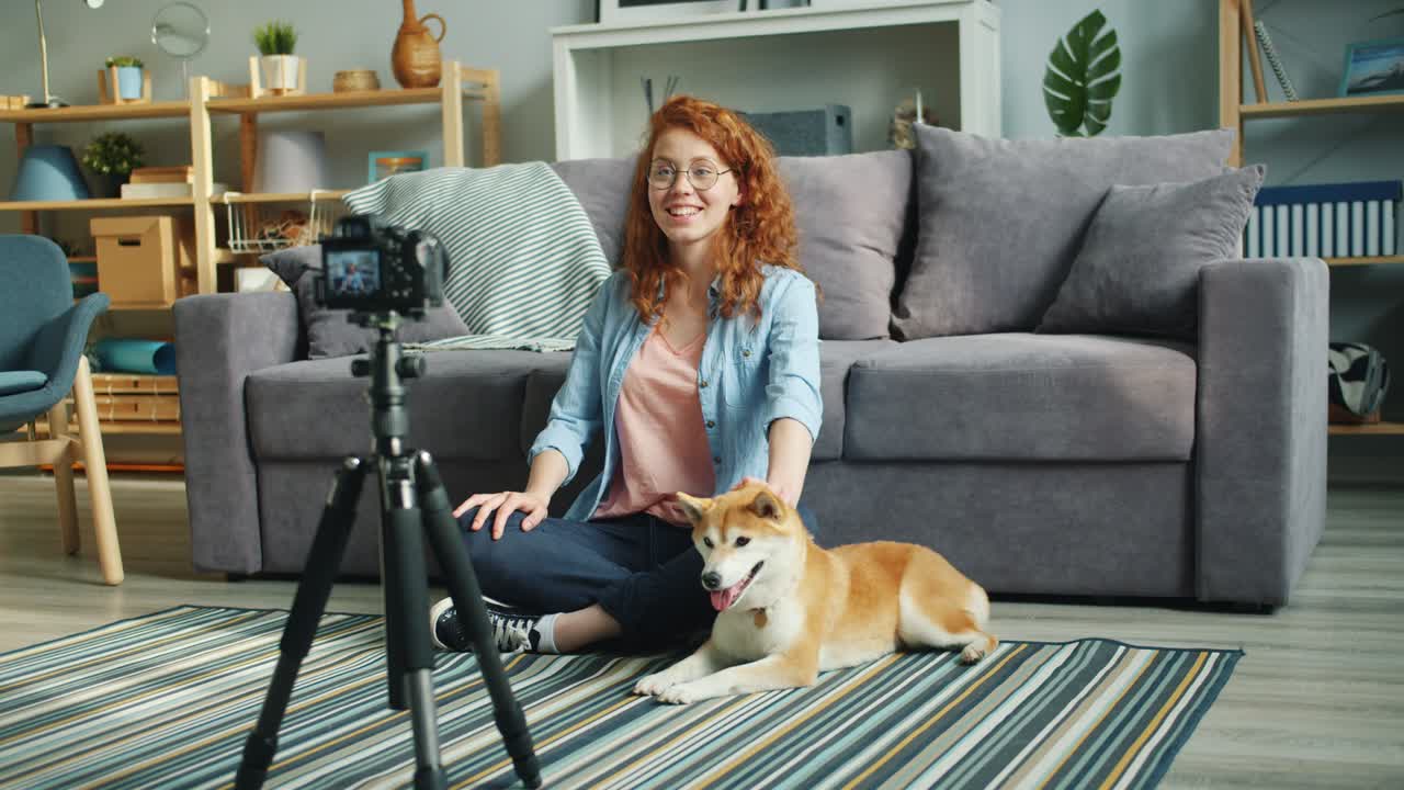 blogger adolescente lindo grabando un videoblog sentado en el suelo en casa con un perro mascota