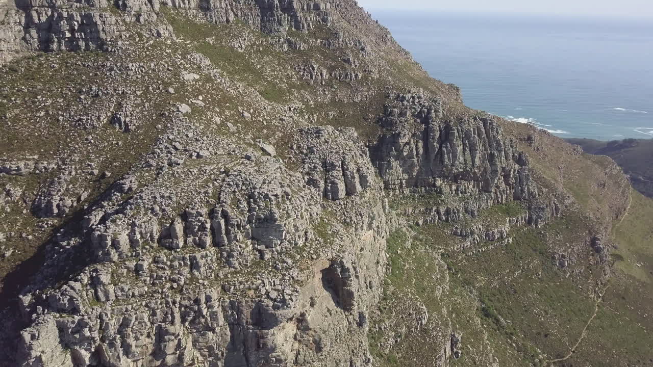 vista aérea escénica de drones que asciende sobre la montaña de la mesa con sus escarpados y majestuosos acantilados rocosos de arenisca contra un océano atlántico azul brillante y un cielo con nubes cirros