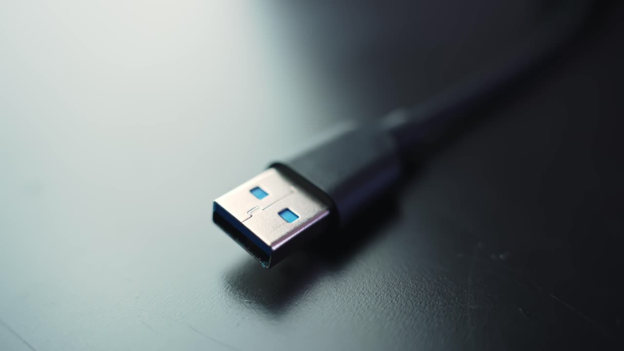 Macro close-up of a USB-A plug on a black cable resting on a dark desk with shallow depth of field and copy space, ideal for tech, charging, and data transfer visuals